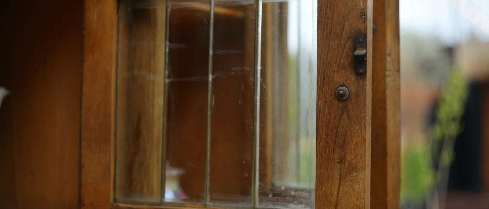 Close-up of a glazed wooden cabinet door standing open on its latch