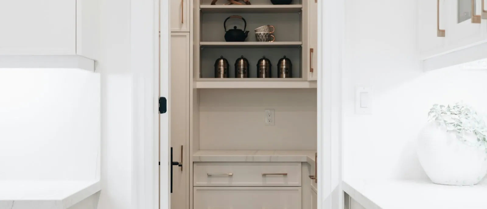 Narrow pantry cabinet seen through a doorway, open shelves of canisters above and drawers below
